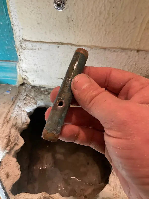 copper-pipe-repair-leak Plumber holding a corroded copper pipe with a pinhole leak removed during pipe repair under a concrete slab