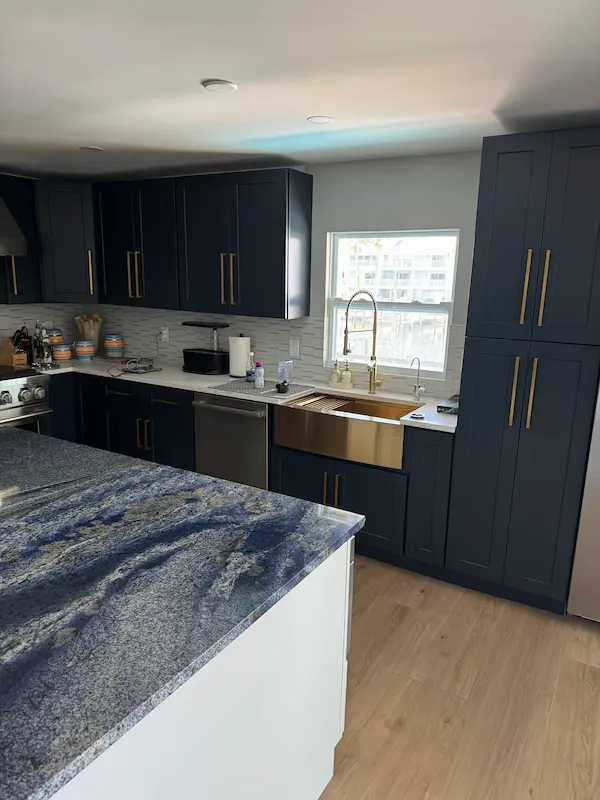 everydayplumber-modern-kitchen-residential-plumbing Modern kitchen with navy cabinets and a brass farmhouse sink, showcasing residential plumbing installation and fixture upgrades.